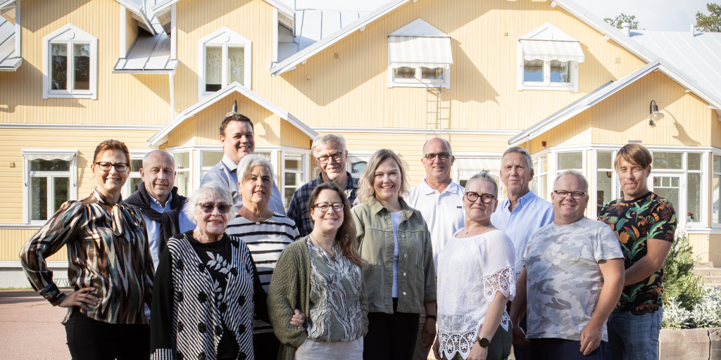 Kommunfullmäktiges ledamöter i grupp framför ett gult hus.